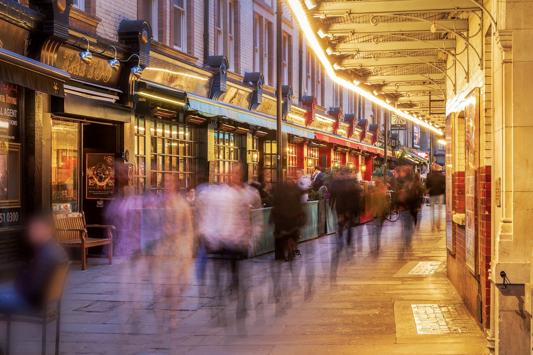 Evening crowds moving through St Martin's Court under a lit canopy